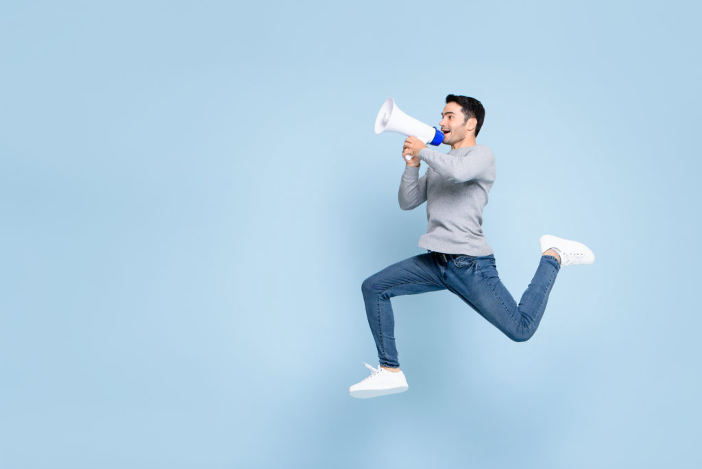 Young active man jumping and shouting on megaphone isolated on light blue background