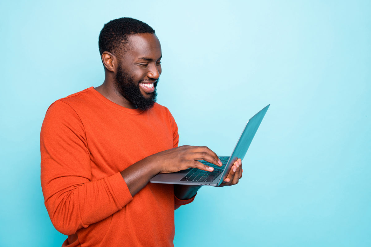 Man in an orange jumper holding a laptop and smiling
