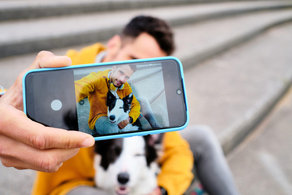 young man takes a picture of himself hugging a border collie dog