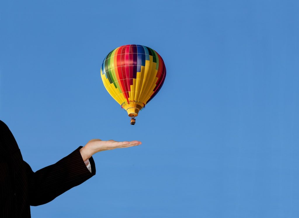 Hand in foregone on a blue background with a hot air balloon behind