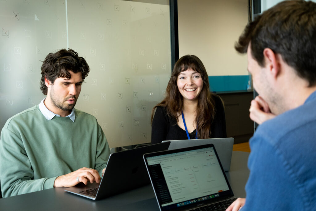 Three colleagues sitting around laptops and smiling