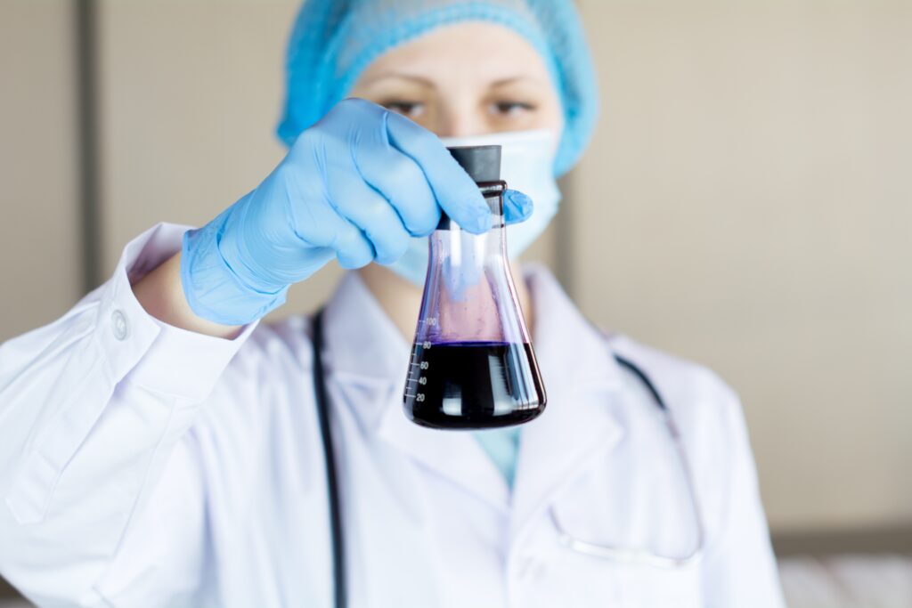 Woman in a lab coat looking at a blue substance in a conical flask
