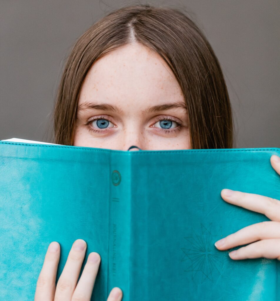 A woman looking over the top of a blue book