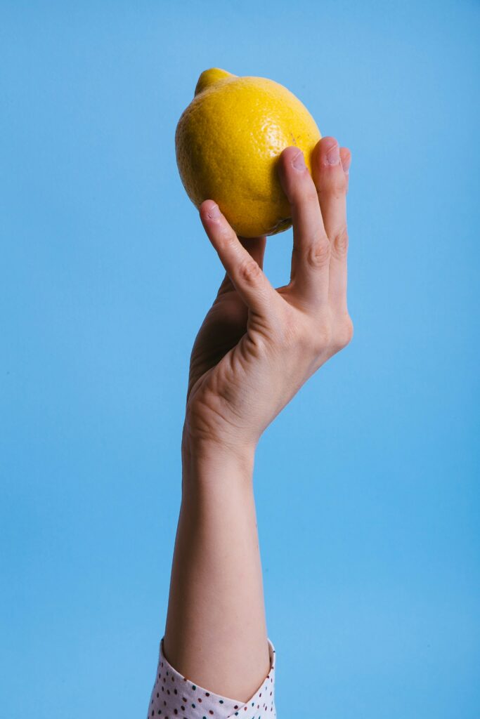 Woman's hand holding a lemon up in the air
