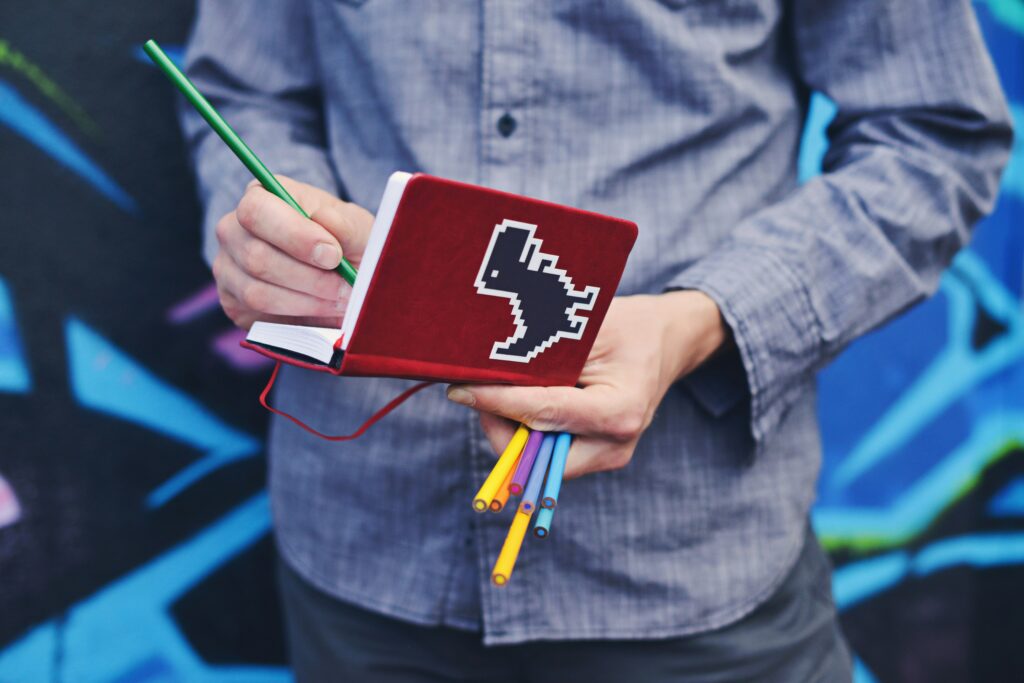 A man in a blue shirt writing in a red notebook