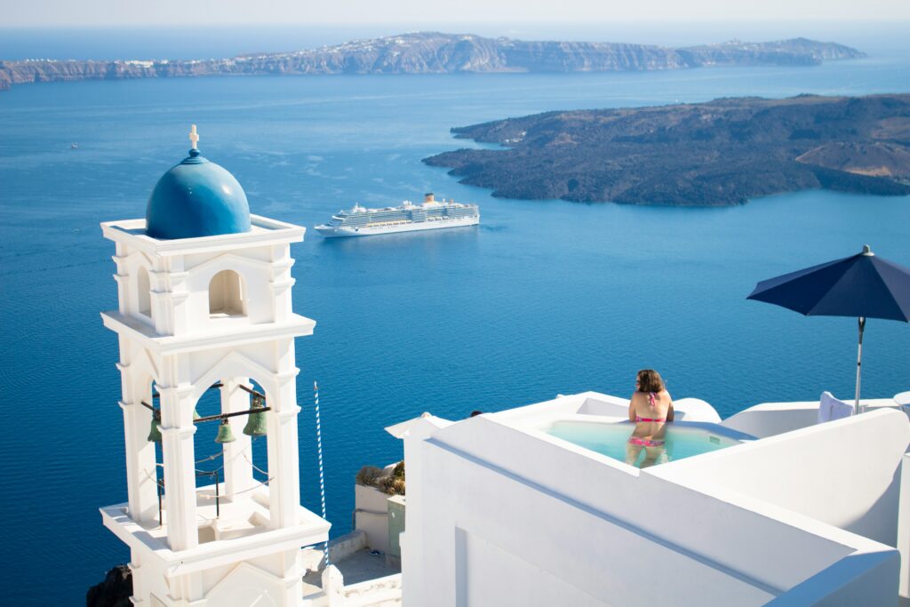 A woman in a bikini looking over the sea from a Greek hotel swimming pool.